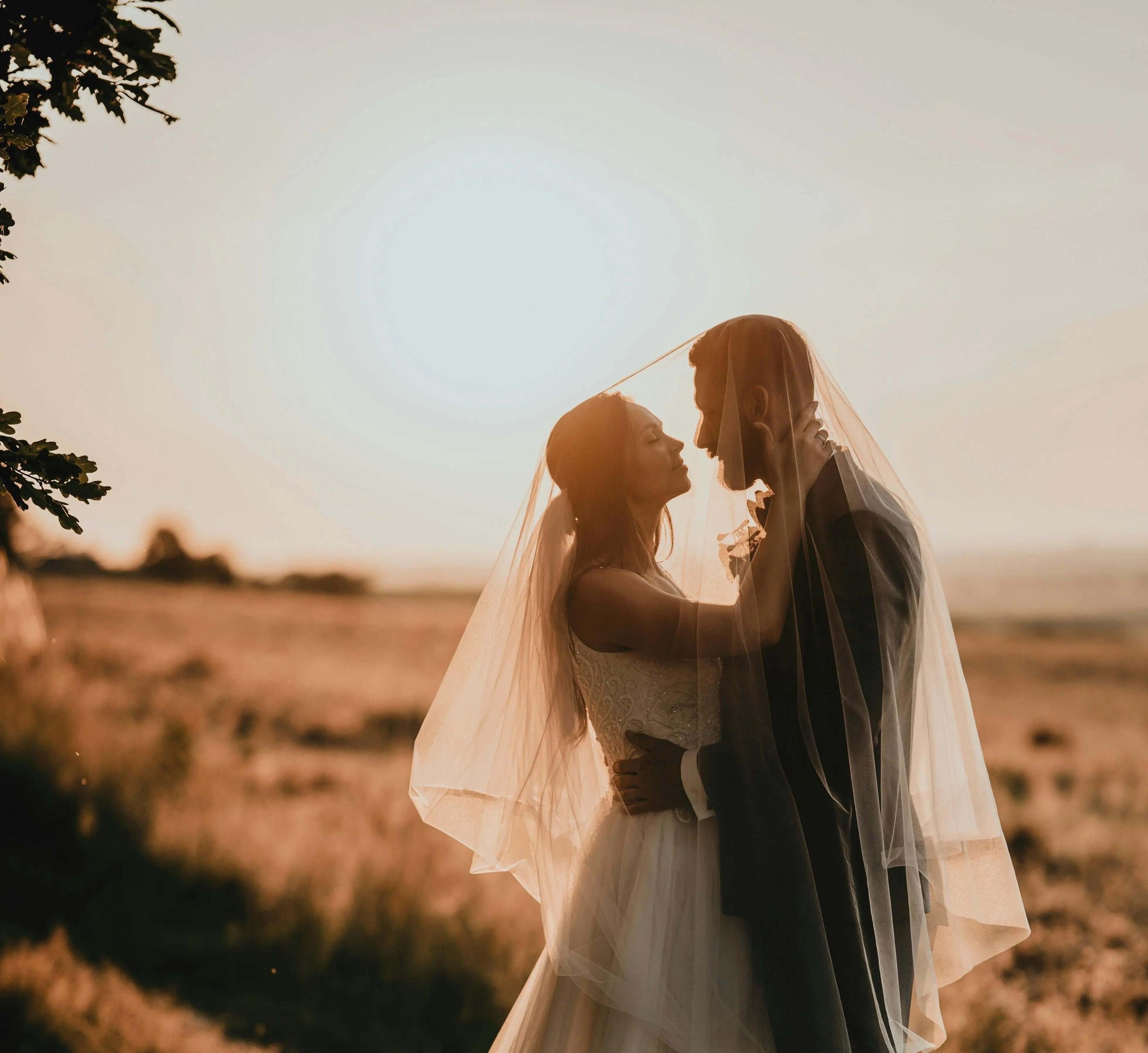 Pareja de novios en su boda mirándose con un paisaje de un campo y de fondo el amanecer