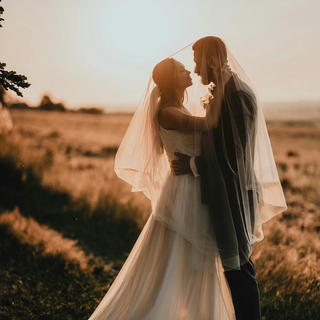 Pareja de novios en su boda mirándose con un paisaje de un campo y de fondo el amanecer