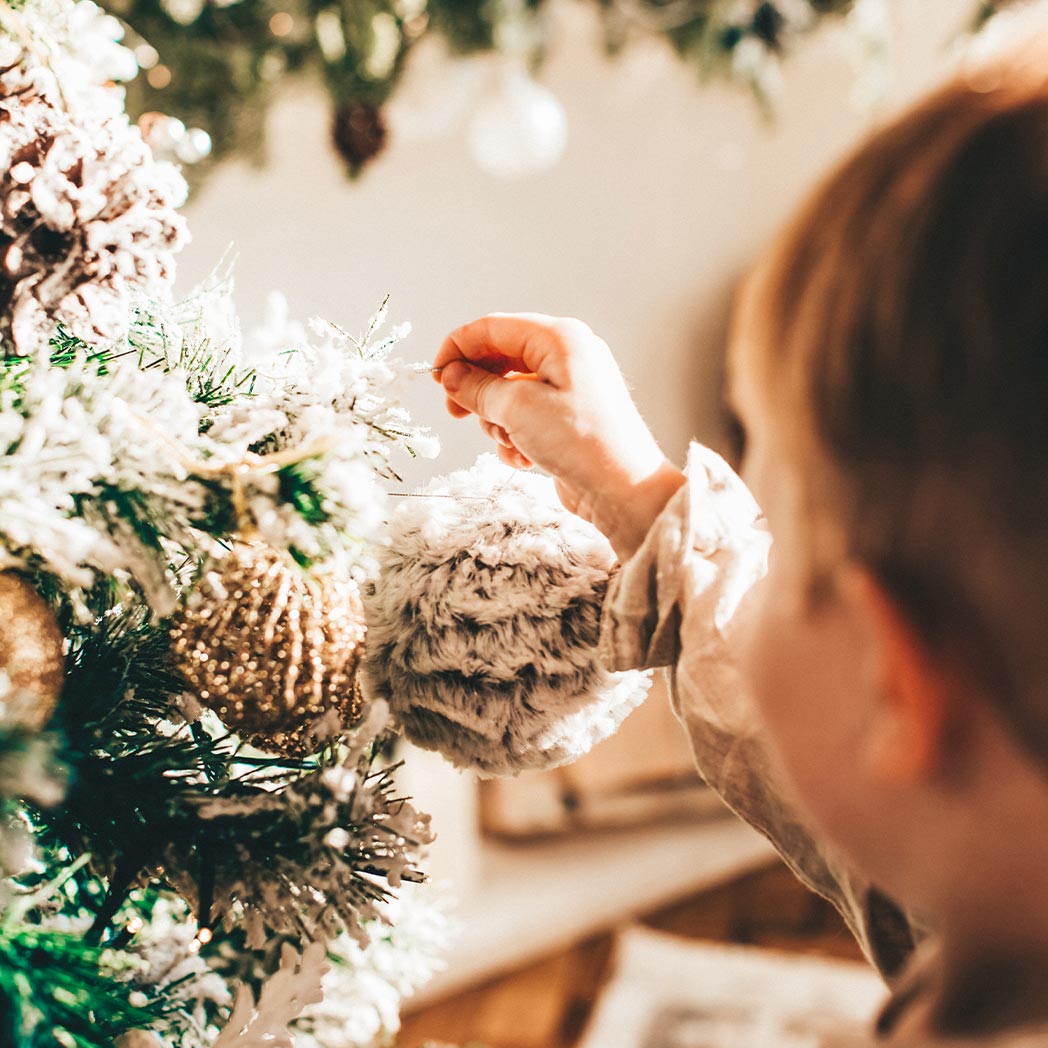 Niño pequeño colocando en el árbol un adorno de Navidad